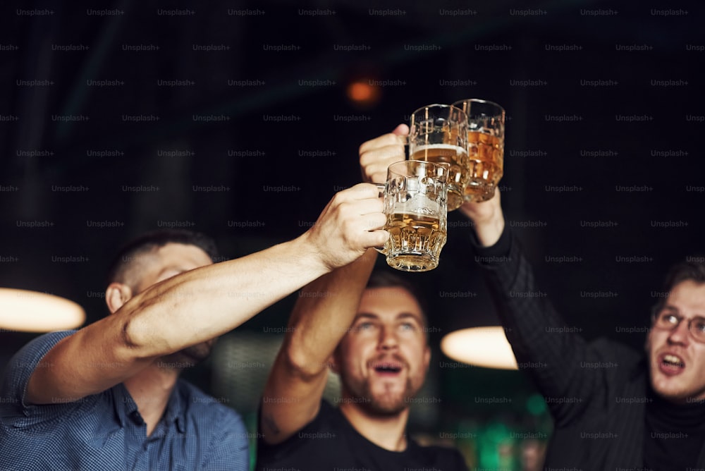 Knocking glasses. Three sports fans in a bar watching soccer. With beer in hands.