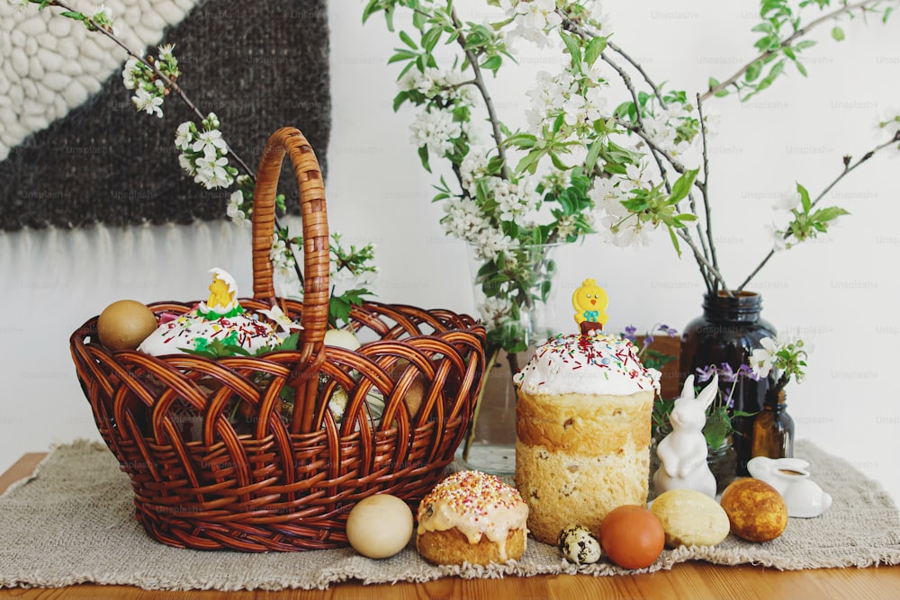 Uova di Pasqua alla moda, pane pasquale fatto in casa, delizioso cibo tradizionale pasquale in cesto di vimini e fiori primaverili che sbocciano su tovagliolo di lino su tavola rustica. Buona Pasqua! Colazione festiva
