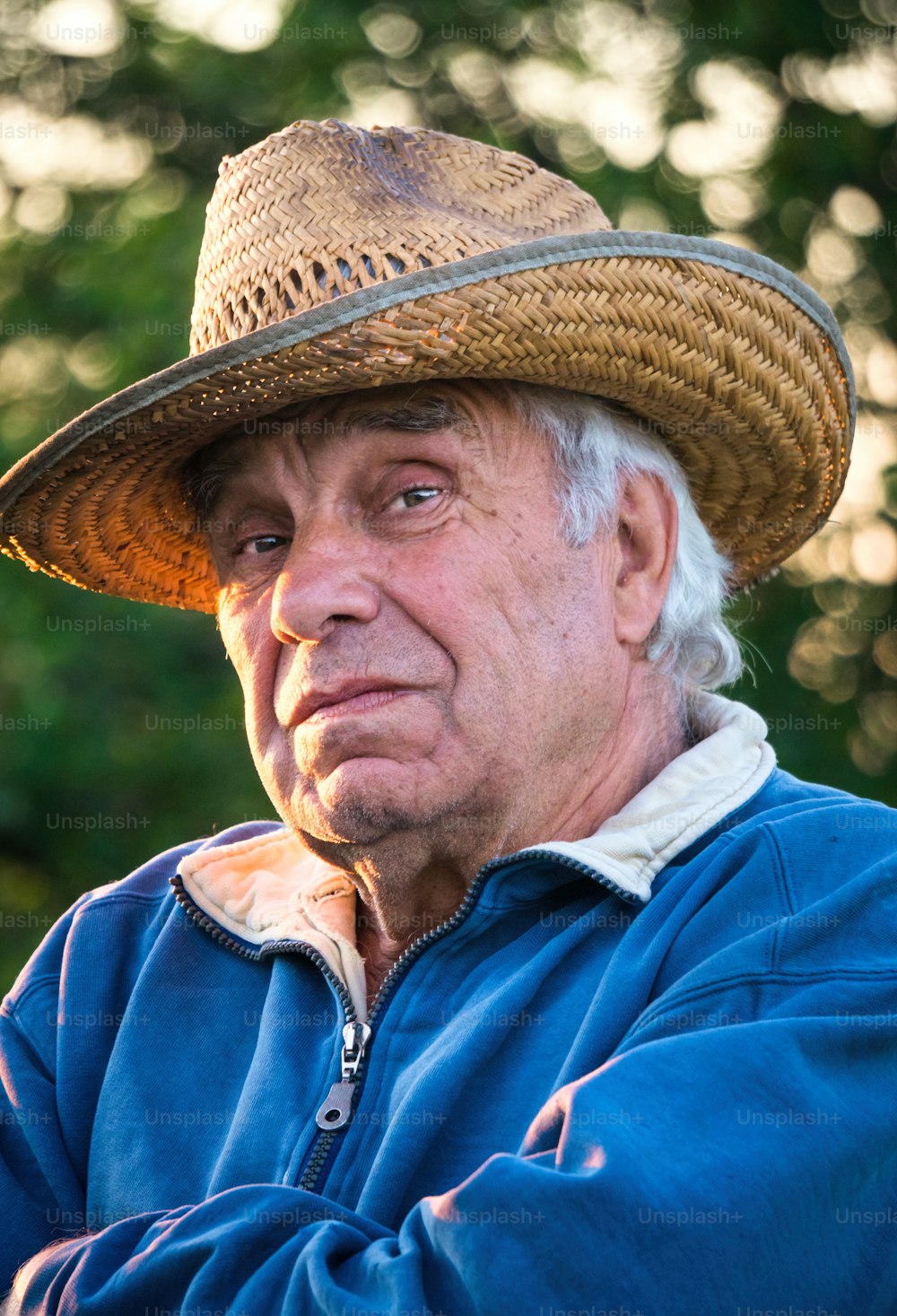 Buona vita da pensionato. Un uomo anziano con un cappello di paglia sullo sfondo di un giardino serale soleggiato. Giardinaggio per il tempo libero