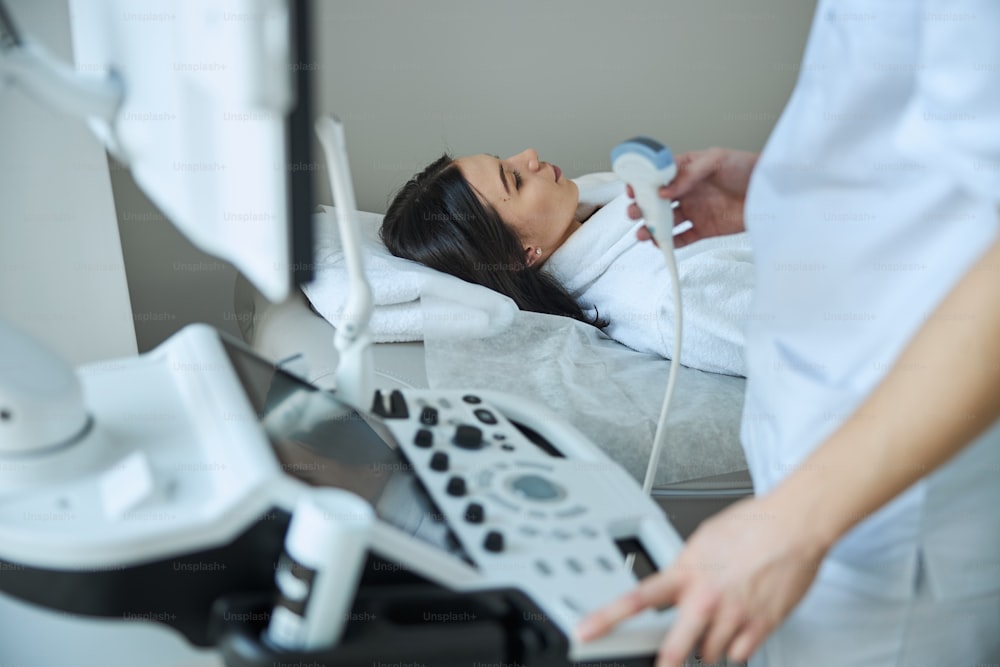 Medico con un trasduttore ad ultrasuoni in mano che inizia un esame ecografico del paziente dai capelli scuri calmo