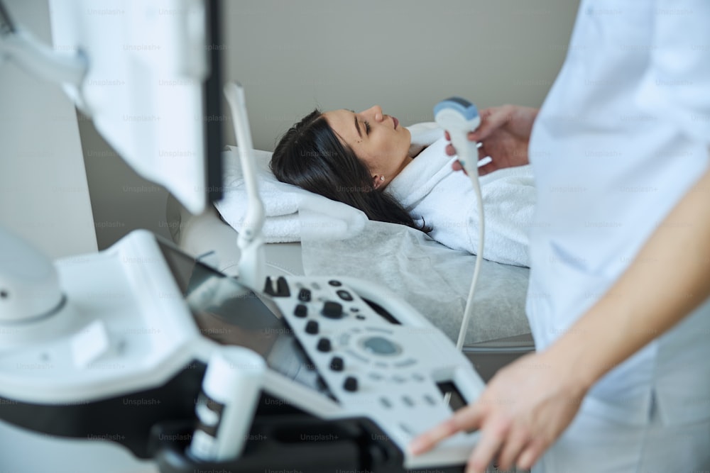 Médico con un transductor ultrasónico en la mano comenzando un examen ecográfico del tranquilo paciente de cabello oscuro