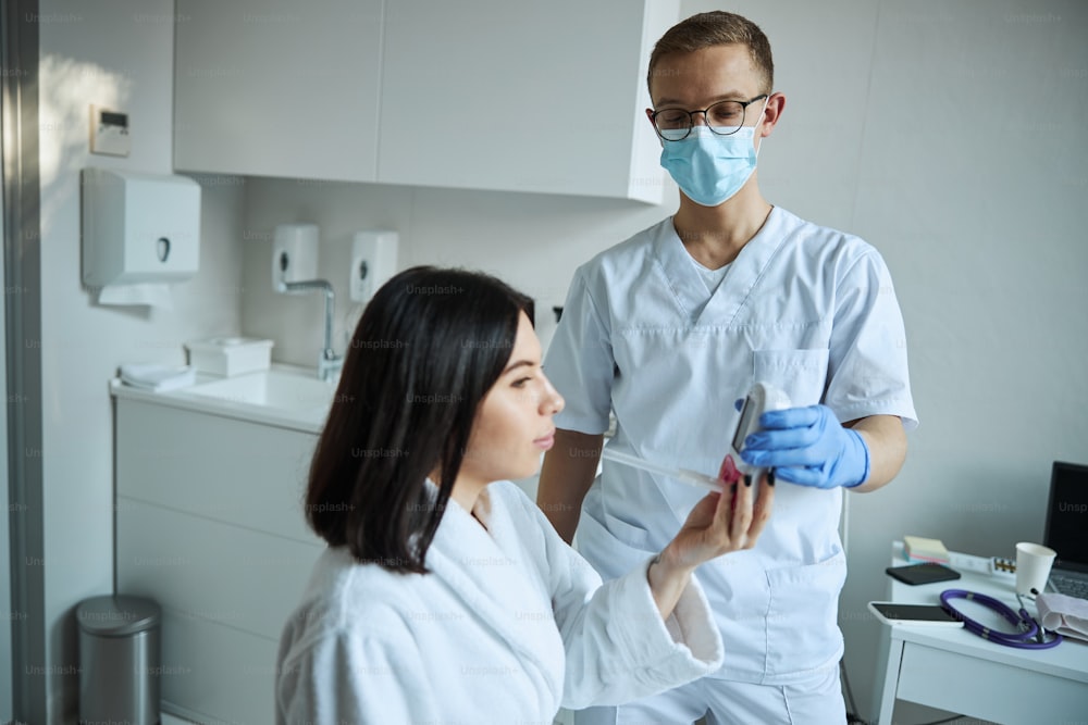 Side view of a serious patient getting a handheld digital spirometer from a male doctor