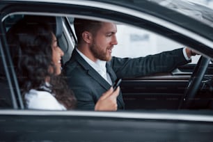 Schönes erfolgreiches Paar, das ein neues Auto im Autosalon ausprobiert.