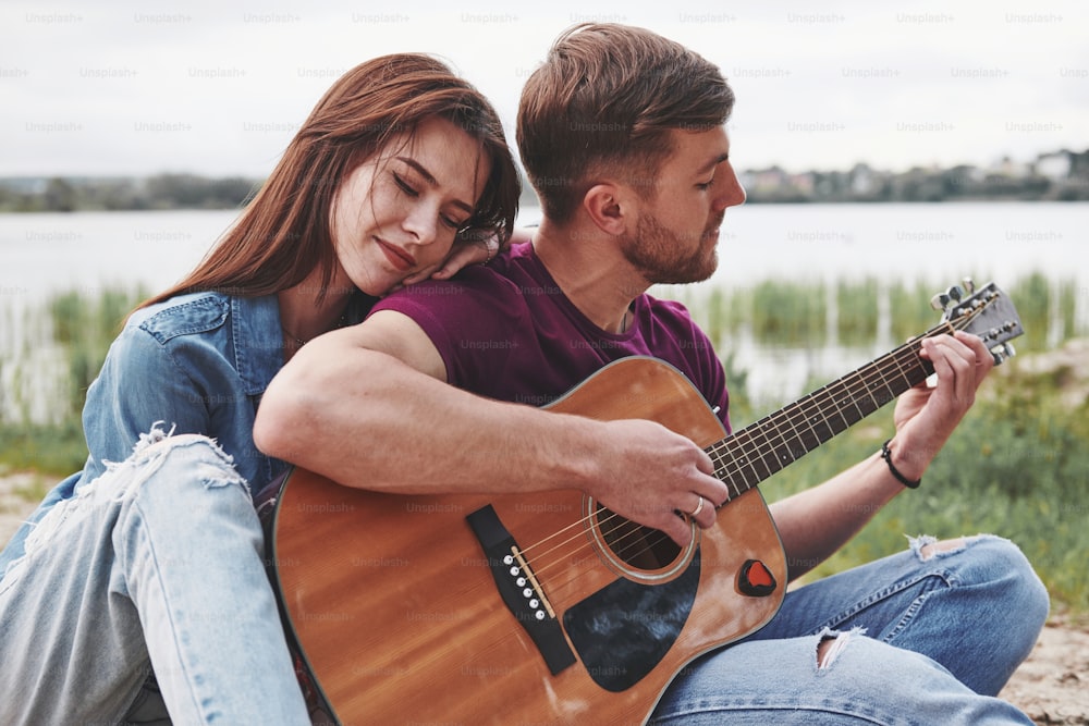 Feeling good. Man plays guitar for his girlfriend at beach on their picnic at daytime.