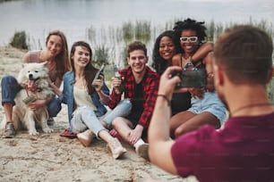 I will take photo of you in a second. Group of people have picnic on the beach. Friends have fun at weekend time.