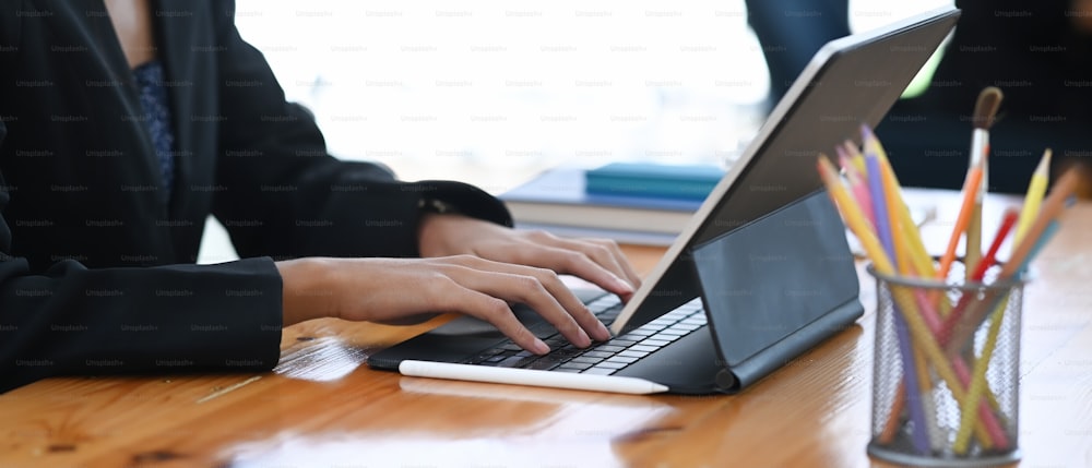 Close up view of businesswoman in suit hands typing on keyboard of computer tablet at office desk.