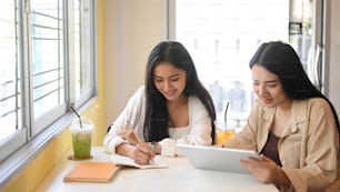 Dos mujeres jóvenes que usan una tableta digital y discuten su proyecto en un café.