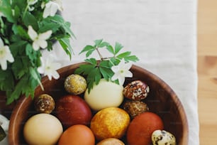 Stylish easter eggs in wooden bowl on rustic table with spring blooming flowers anemones. Space for text. Natural dyed eggs in yellow and red colors. Happy Easter!
