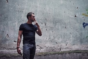 Retrato do homem na camisa preta fumando no fundo da parede rachada velha.