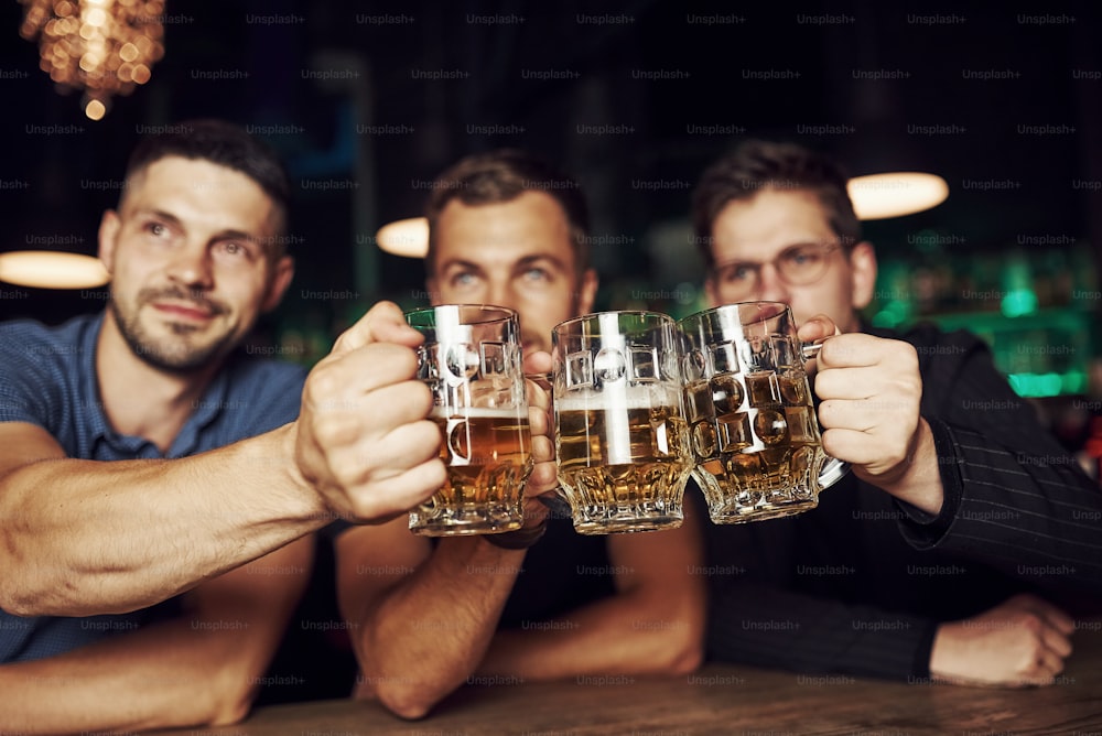 Klopfende Gläser. Drei Sportfans in einer Bar schauen Fußball. Mit Bier in den Händen.