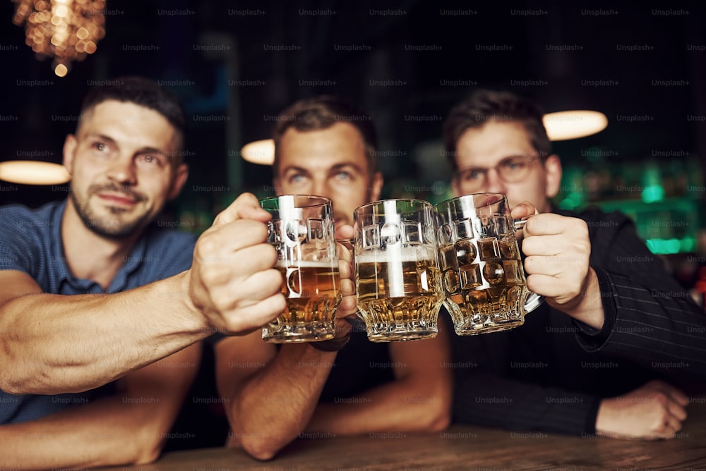 Golpeando vasos. Tres aficionados al deporte en un bar viendo fútbol. Con cerveza en la mano.