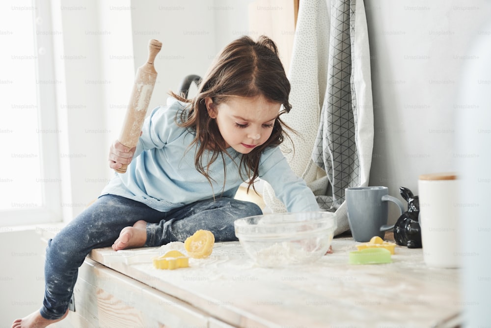 Non lasciare i tuoi figli da soli a casa, possono preparare del cibo. Foto di una graziosa bambina che si siede sul tavolo della cucina e gioca con la farina.