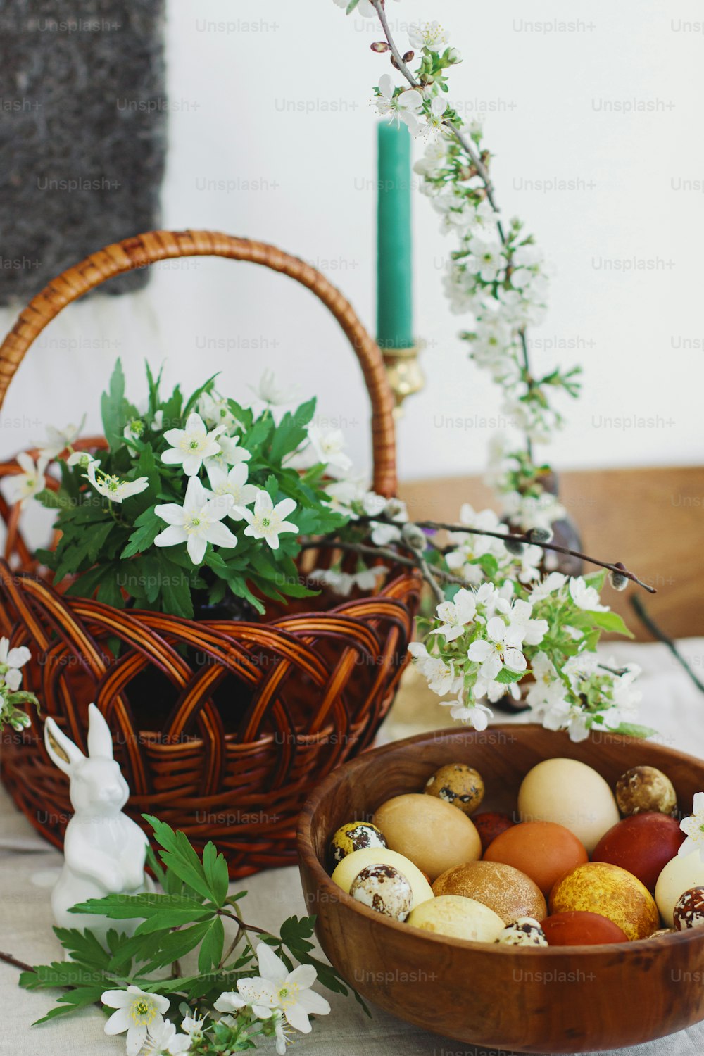 토끼 인형, 고리 버들 바구니, 촛불, 봄에 피는 꽃이 있는 소박한 테이블에 나무 그릇에 담긴 세련된 부활절 달걀. 행복한 부활절! 노란색과 빨간색의 자연 염색 계란