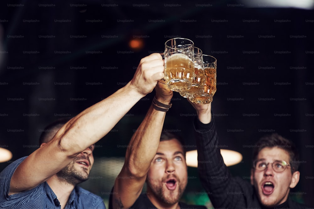 Klopfende Gläser. Drei Sportfans in einer Bar schauen Fußball. Mit Bier in den Händen.