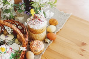 Des œufs de Pâques élégants, du pain de Pâques fait maison, de délicieux plats traditionnels de Pâques dans un panier en osier et des fleurs printanières épanouies sur une serviette en lin sur une table rustique. Joyeuses Pâques ! Petit-déjeuner festif