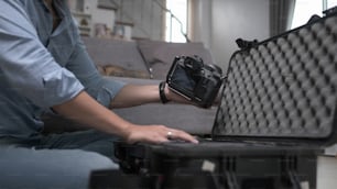 Cropped shot of male photographer putting digital camera into big bag with other gadgets.