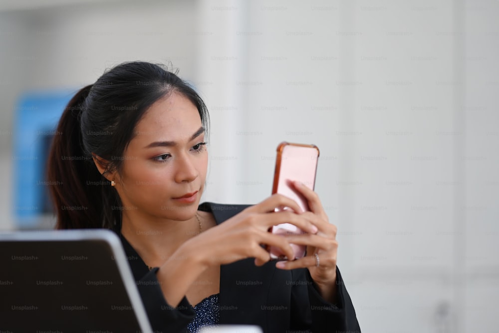 Attraktive Geschäftsfrau, die ein Smartphone nutzt und soziale Medien überprüft, während sie im Büro sitzt.