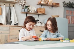 Just having free time. Two kids playing with yellow and orange toys in the white kitchen.
