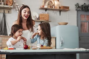 Process of eating. Young beautiful woman give the cookies while they sitting near the table with toys.