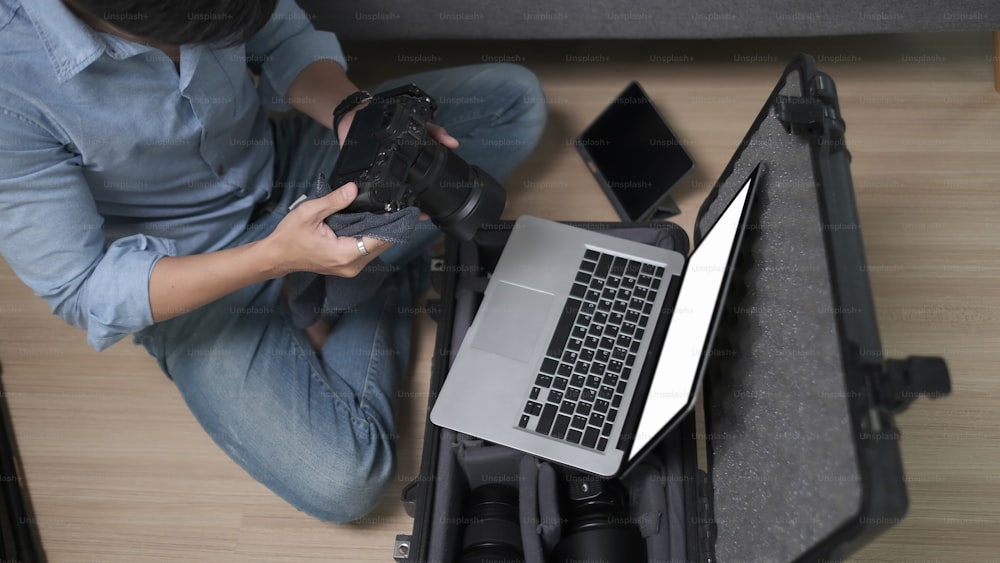 Vue aérienne d’un photographe masculin vérifiant des images sur un appareil photo numérique alors qu’il est assis sur le plancher en bois du studio.