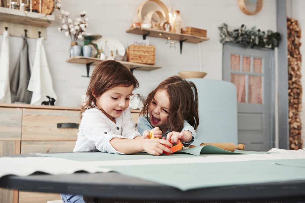 Happy childhood. Two kids playing with yellow and orange toys in the white kitchen.