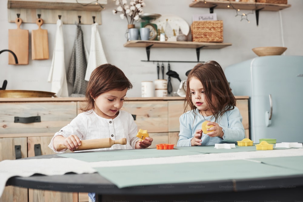 Two kids playing with yellow and orange toys in the white kitchen.