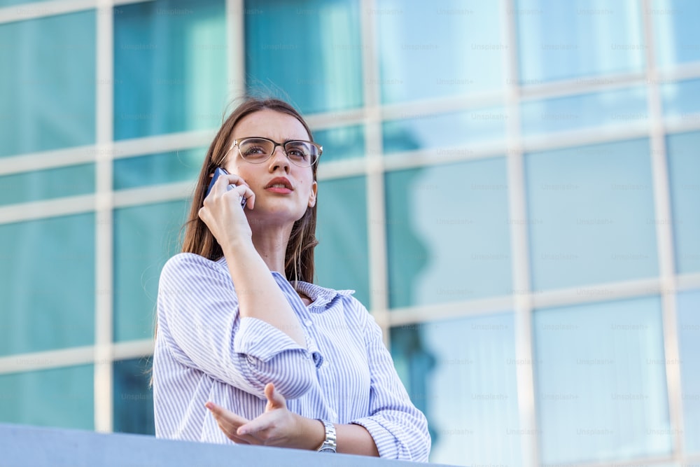 Smart successful business woman, financial representative, legal attorney, consultant, modern professional talking on mobile phone in front of windows in an office building