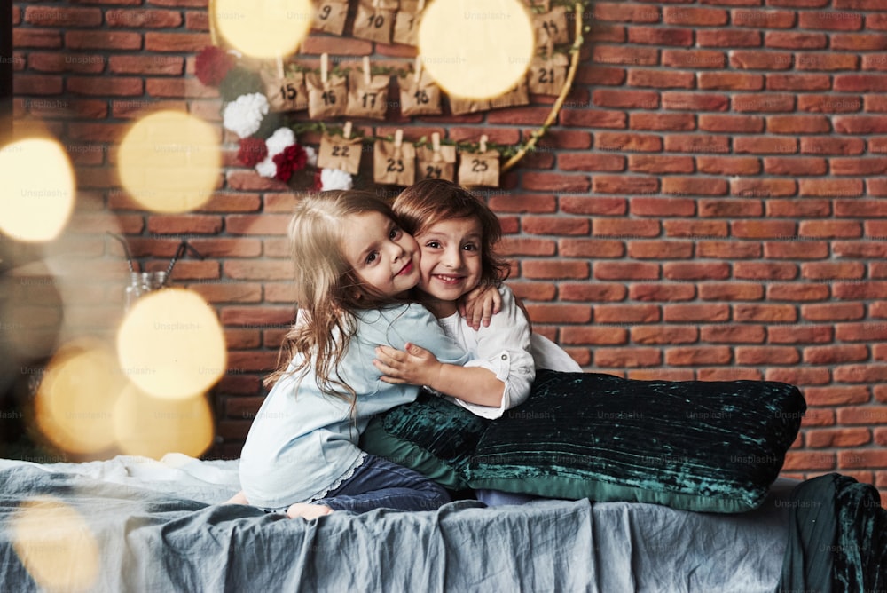 Abbracci amichevoli. Bambine che si divertono sul letto con interni di vacanza sullo sfondo.