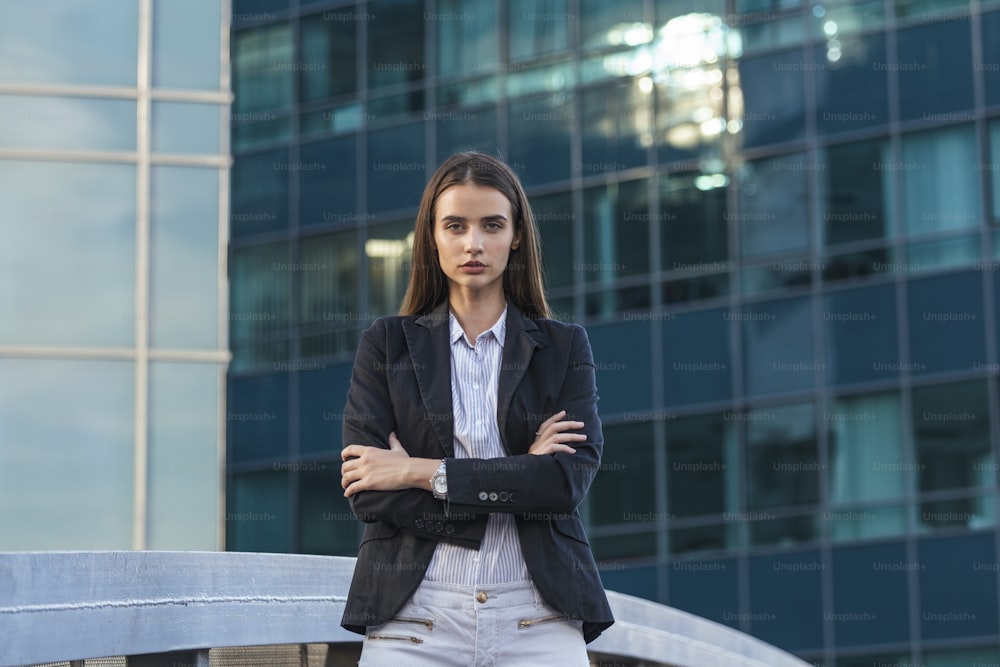 Successful female office worker with net-book is standing in skyscraper interior against big window with city view on background. Proud woman architect looking satisfied with completed project