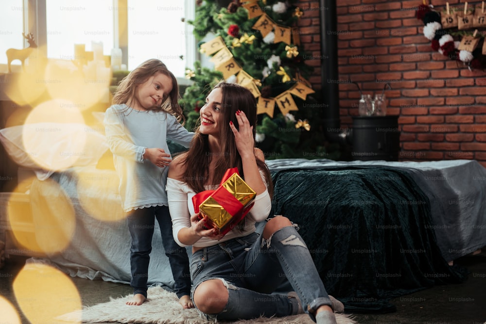 Family happiness. Mother and daughter sits in holiday decorated room and holds gift box.
