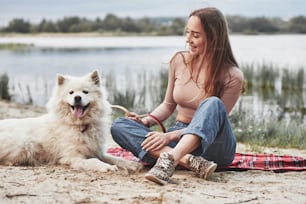Happy animal. Blonde girl with her cute white dog have a great time spending on a beach.