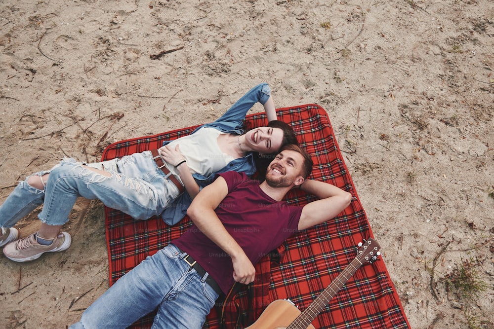 Top view. Young couple have picnic on the beach. Lying on the red colored blanket.