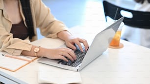 Cropped shot of young woman hands typing on laptop computer and sitting in coffee shop.