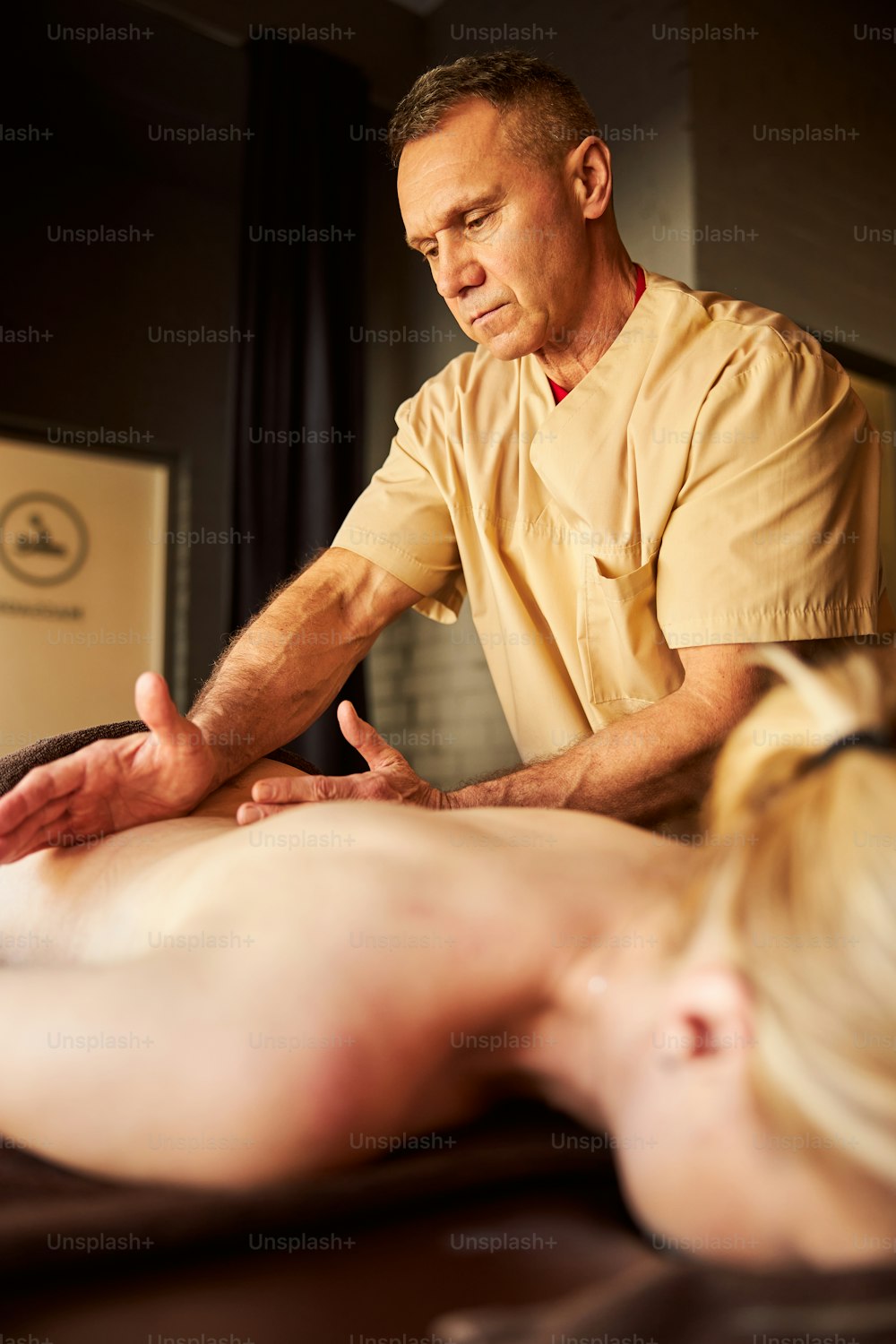 Focused spa worker looking concentrated while rubbing and pressing on person bare back