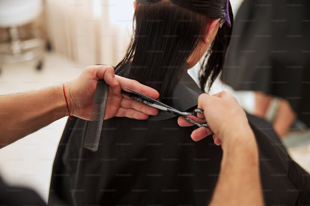Photo recadrée d’un coiffeur coupant les pointes de cheveux mouillées de la cliente à l’aide d’un peigne et d’une paire de ciseaux