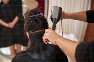 Vista posteriore di una donna dai capelli scuri che si fa acconciare i capelli da un coiffeur usando un paio di strumenti da parrucchiere