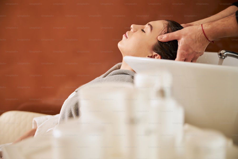 Relaxed lady with her head leaned back into the sink lying with her eyes closed at a beauty salon