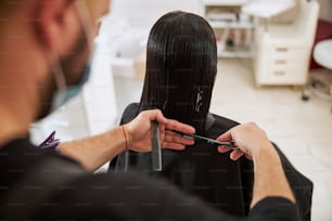 Back view of a stylist with a comb and scissors in his hands cutting the woman split ends