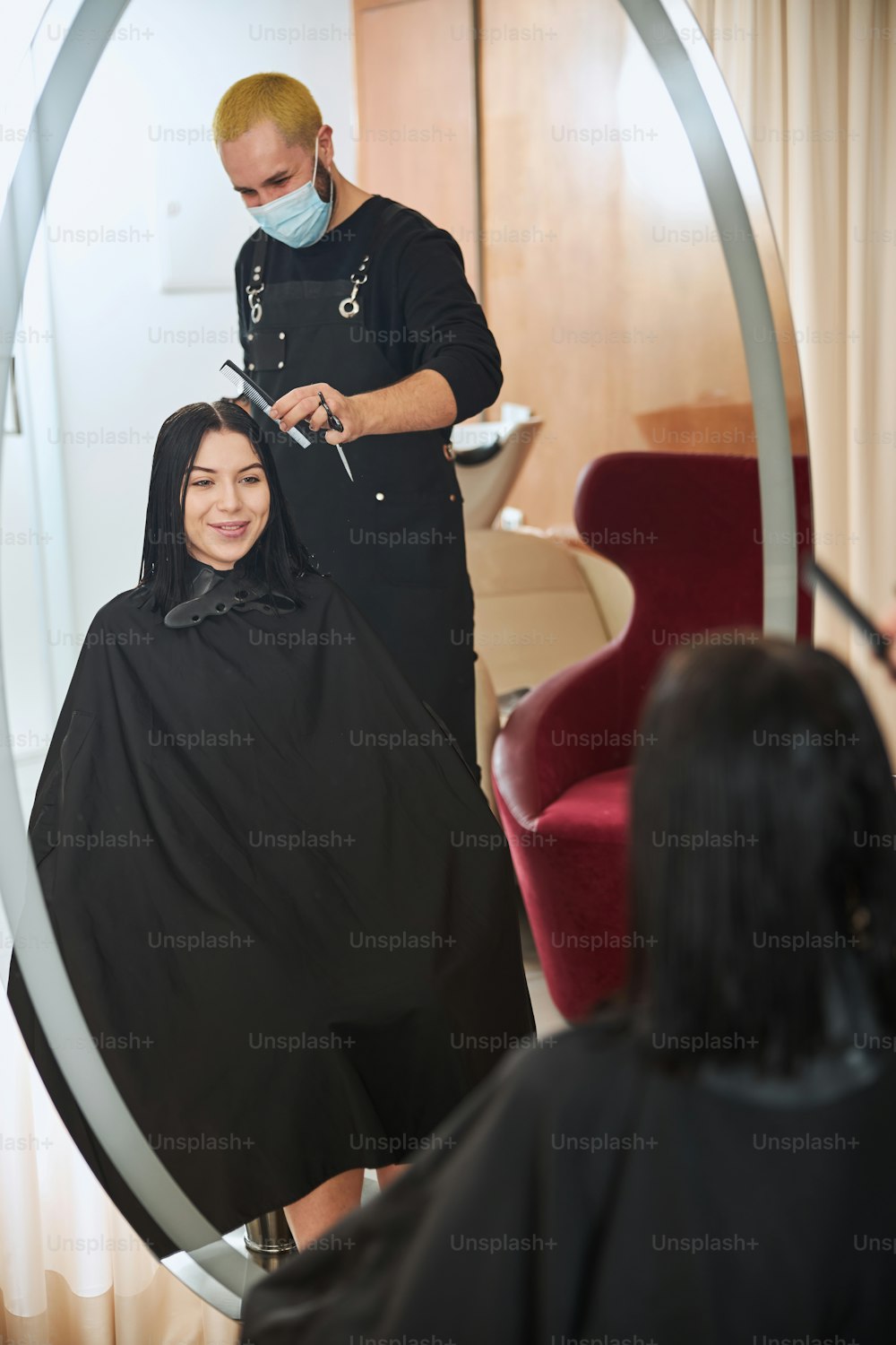 Lächelnd erfreut gut aussehende junge dunkelhaarige kaukasische Frau, die sich während des Haarstylings im Spiegel betrachtet