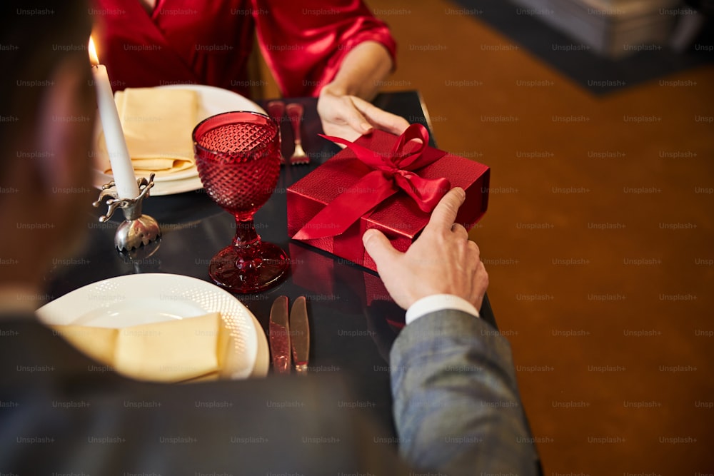 Cropped photo of unrecognised man in suit giving a red gift box to a lady in front of him