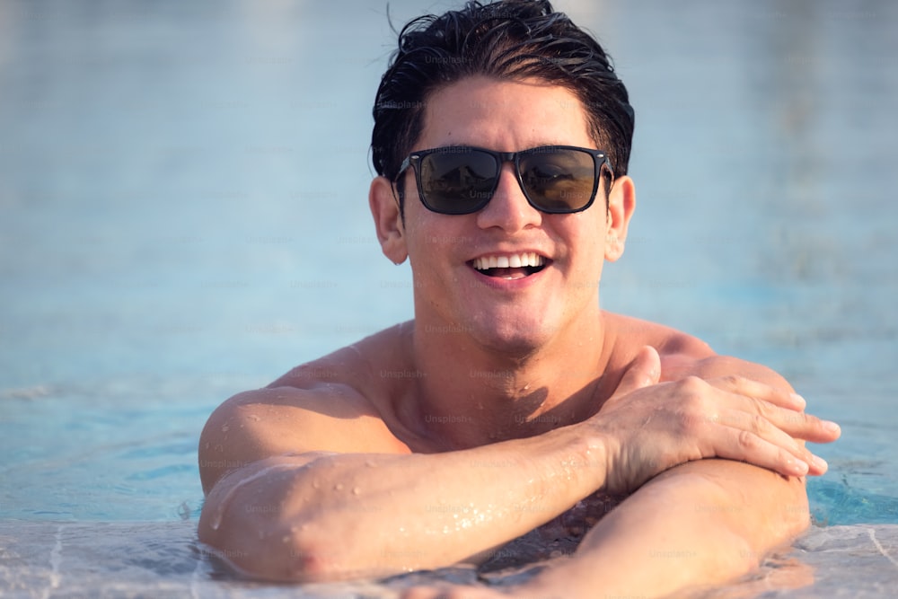 Close up portrait of attractive young man in sunglasses resting on edge of swimming pool