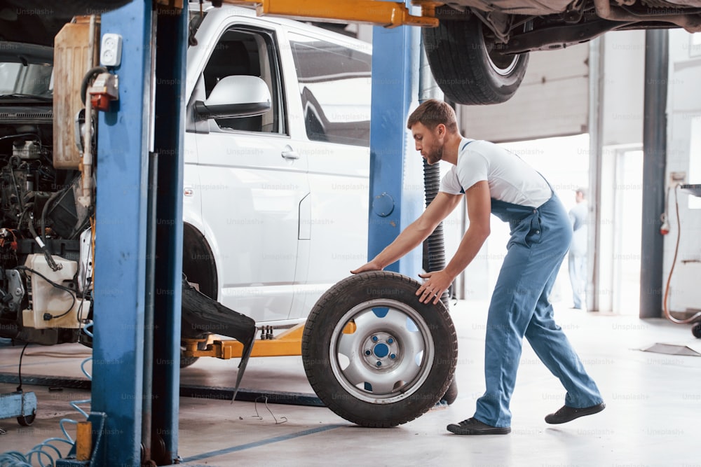 Rolling tire. Employee in the blue colored uniform works in the automobile salon.