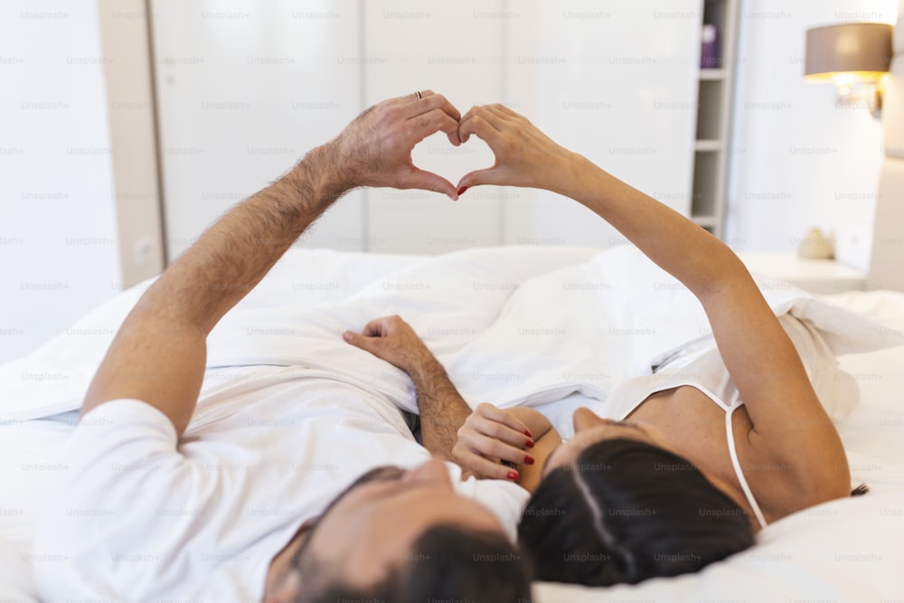 Coppia sdraiata sul letto che forma forma a forma di cuore con la mano