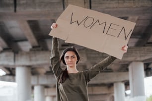 Sozinho na área. Menina bonita em roupas casuais fica com cartaz feminista feito à mão nas mãos.