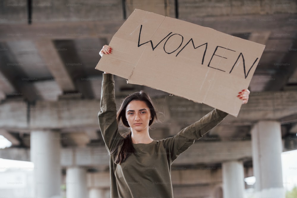 Da solo nella zona. La bella ragazza in abiti casual sta in piedi con un poster femminista fatto a mano tra le mani.