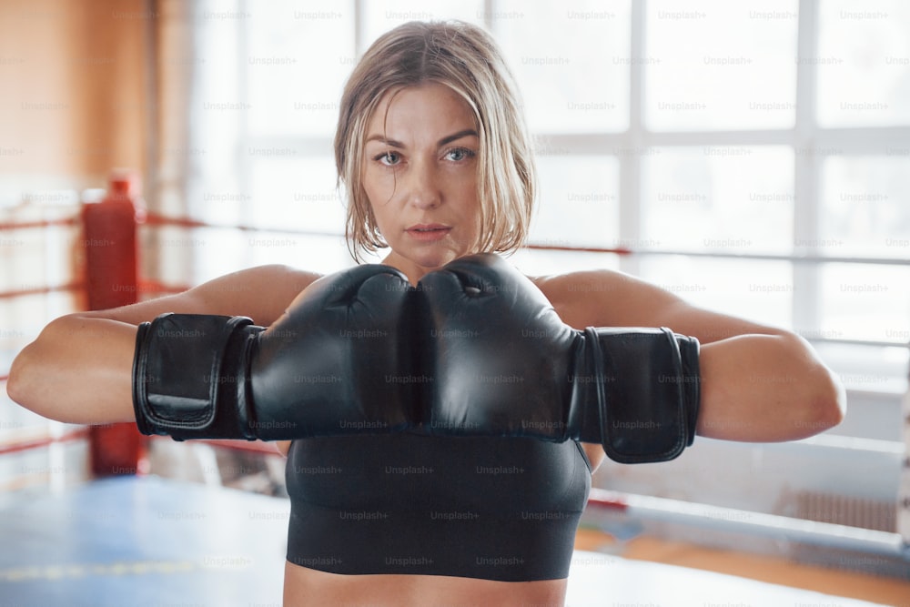Confident strong woman. Female training in the boxing ring. In black colored clothes.