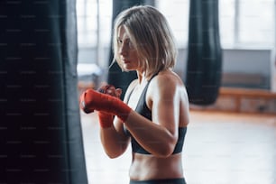 Workout strokes. Female boxer is punching the bag. Blonde have exercise in the gym.