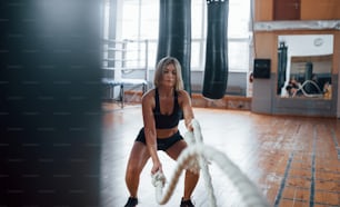 Reflection in the mirror. Blonde sport woman have exersice with ropes in the gym. Strong female.