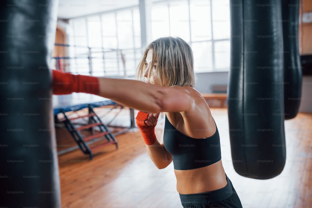 Left hand kick. Female boxer is punching the bag. Blonde have exercise in the gym.