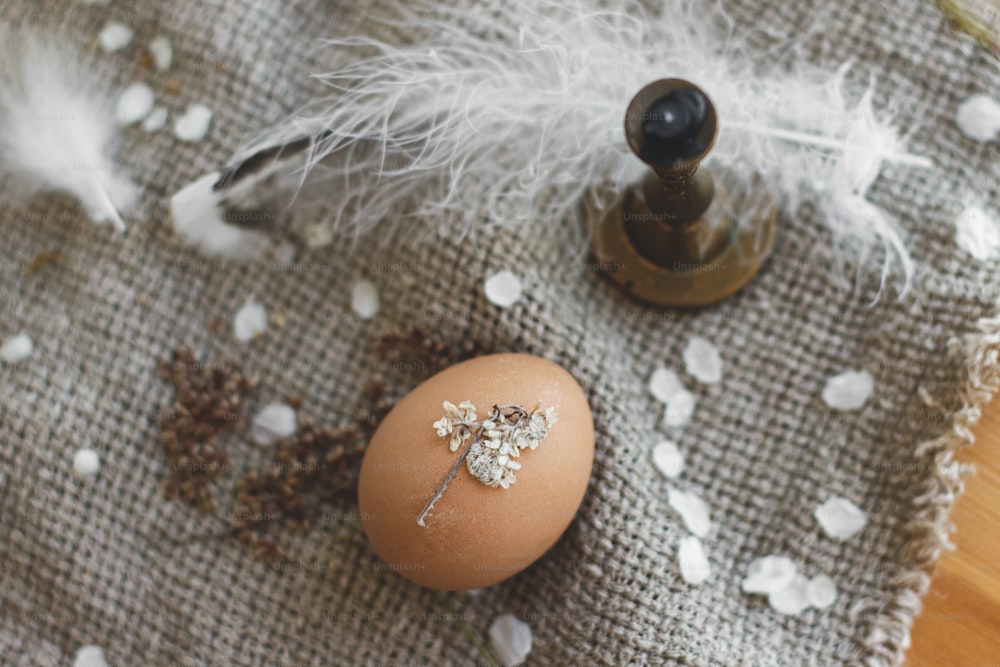 Huevo de Pascua decorado con pétalos de flores secas sobre fondo de servilleta de lino rústico, vela y pluma. Decoración ecológica natural creativa de huevos de pascua. Felices Pascuas. Vista superior